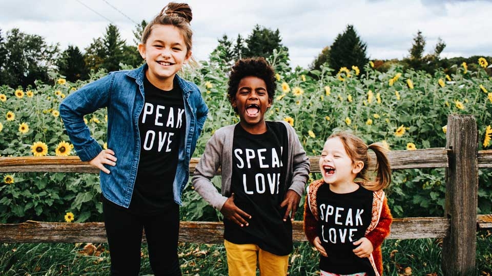 Three children wearing speak love t-shirts standing in a sunflower field