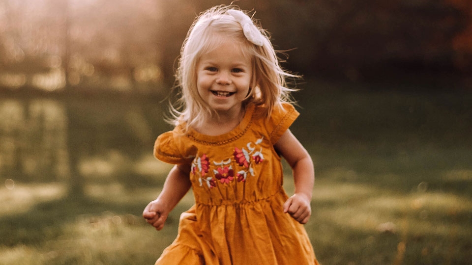 A preschool aged girl with blonde hair and wearing an orange dress running in a field